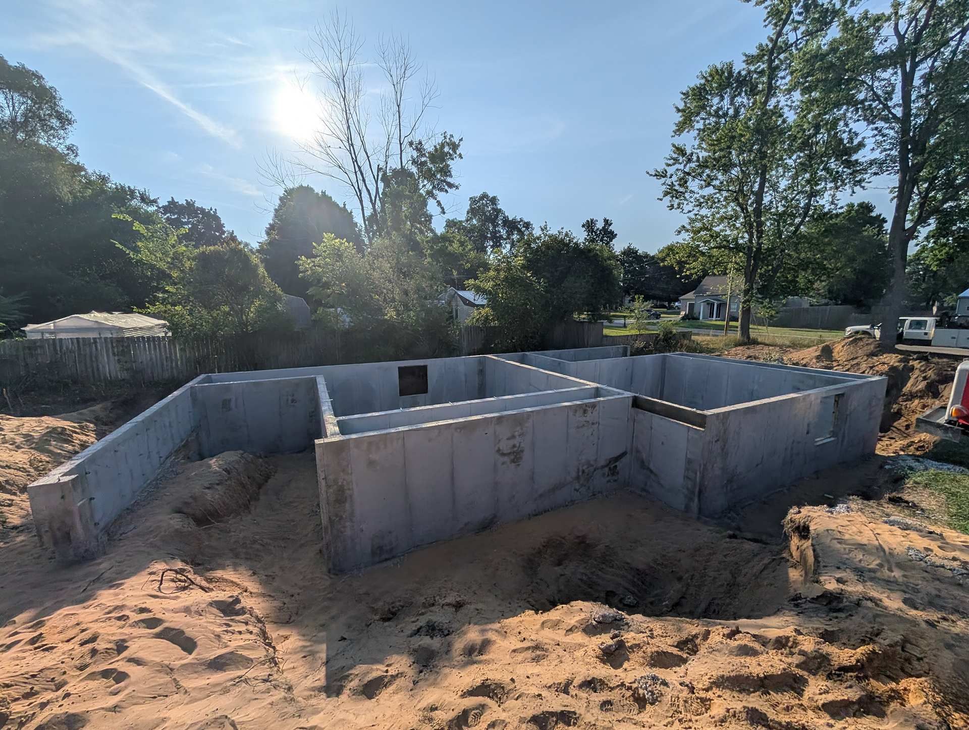 Concrete foundation walls for a new house under construction on a sandy lot under a bright, sunny sky.