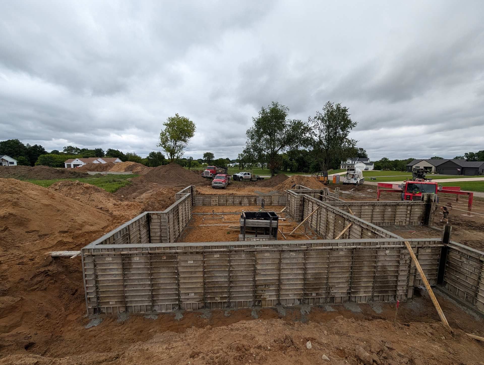 A concrete foundation for a new house under construction on a dirt lot under a cloudy sky.