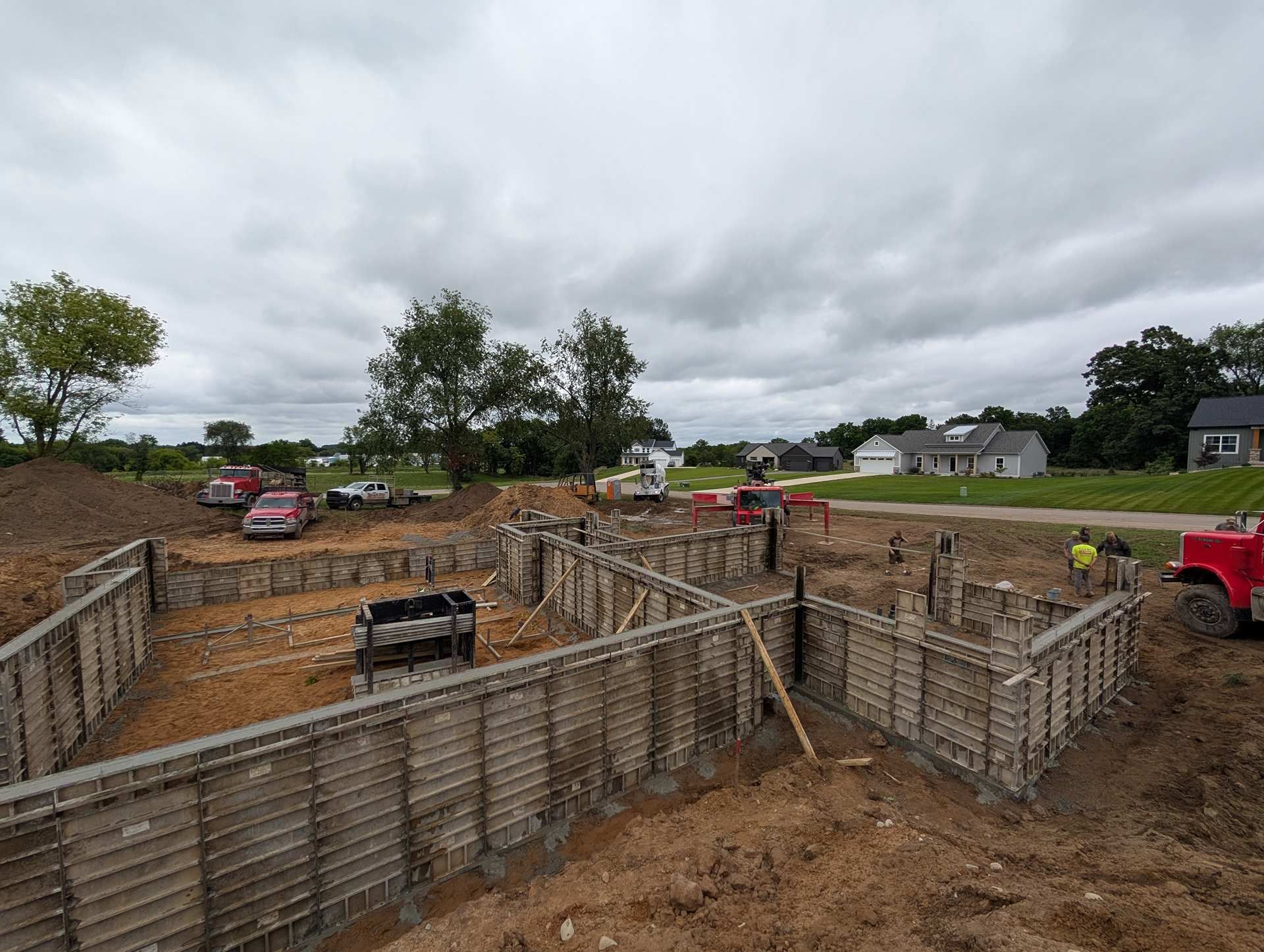 A construction site showing concrete foundation forms for a new house under a cloudy sky.