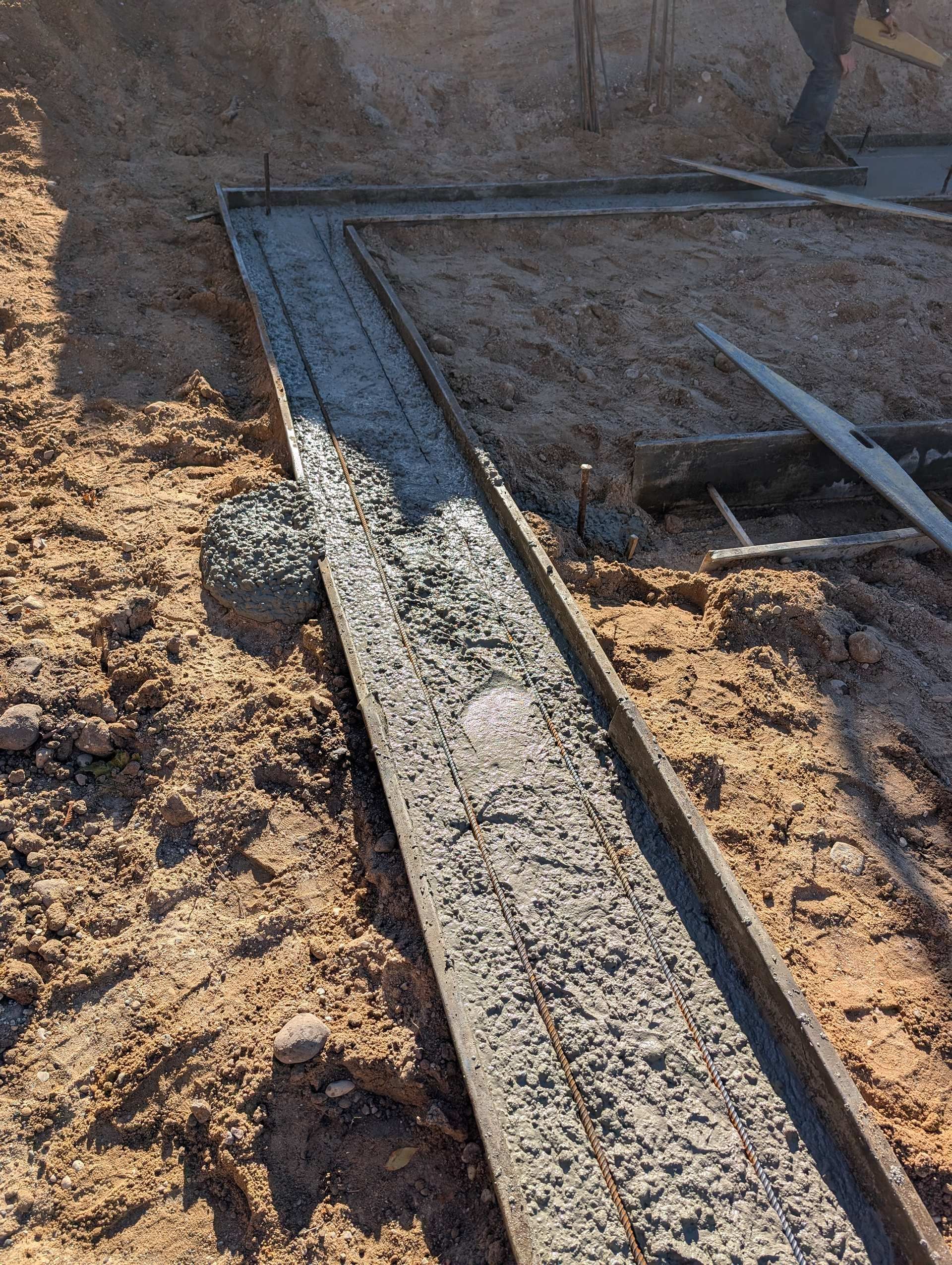 Freshly poured concrete footings set within wooden forms on a dirt construction site.