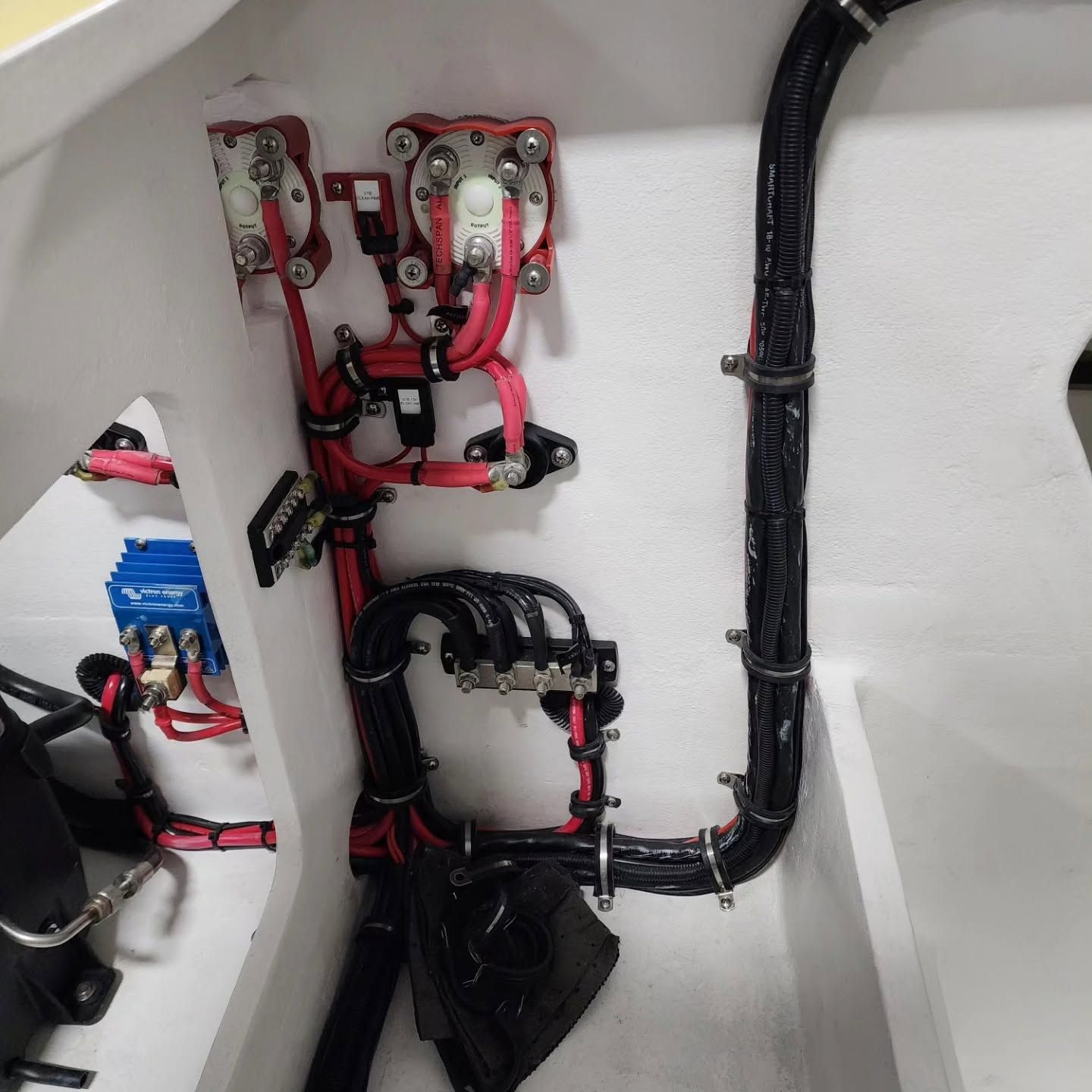 Red and black electrical wiring and components mounted inside a white compartment.