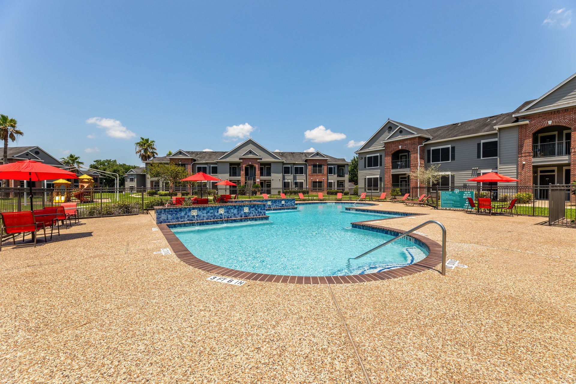 Apartment pool with turquoise umbrellas beside brick buildings on a sunny day