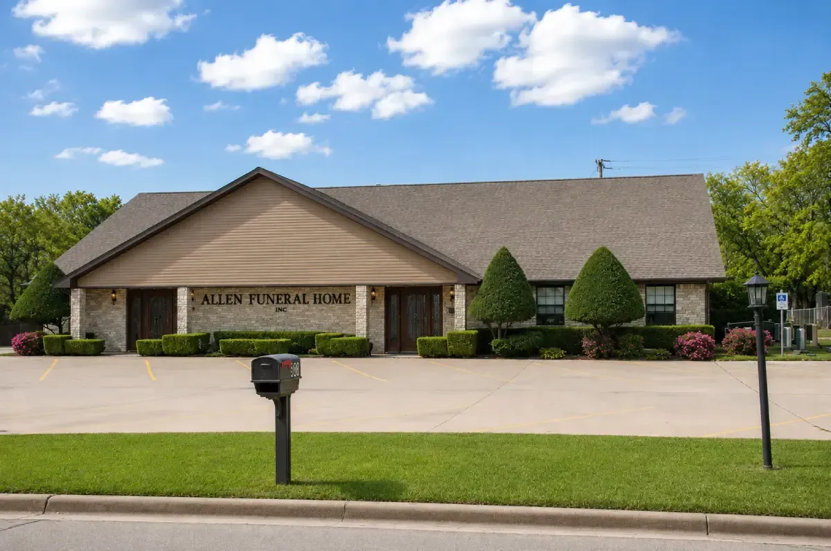 Single-story beige brick building with a sign, manicured shrubs, and a mailbox beside a paved street.