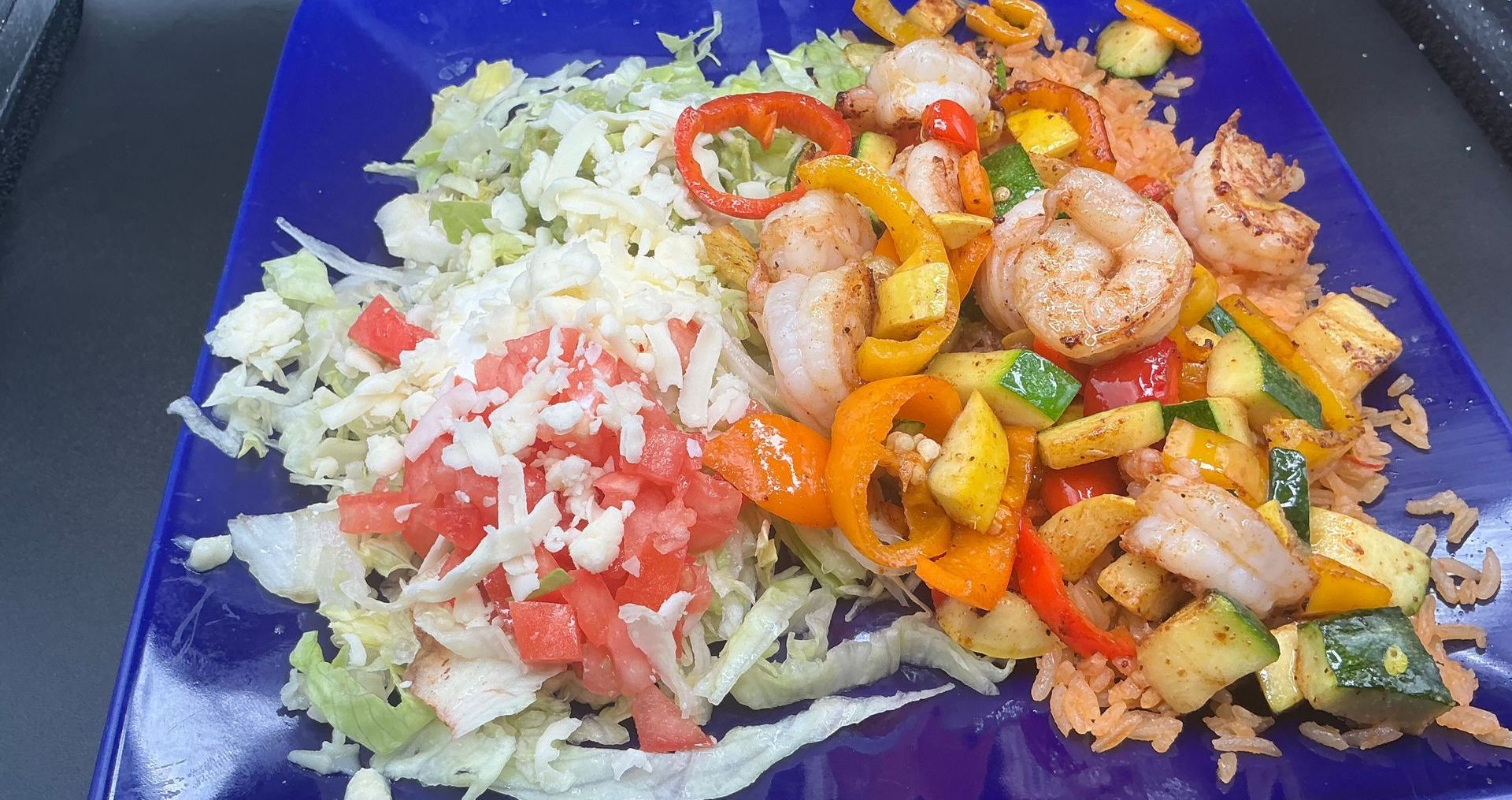 Shrimp fajita platter with rice, vegetables, and shredded lettuce on a blue plate.