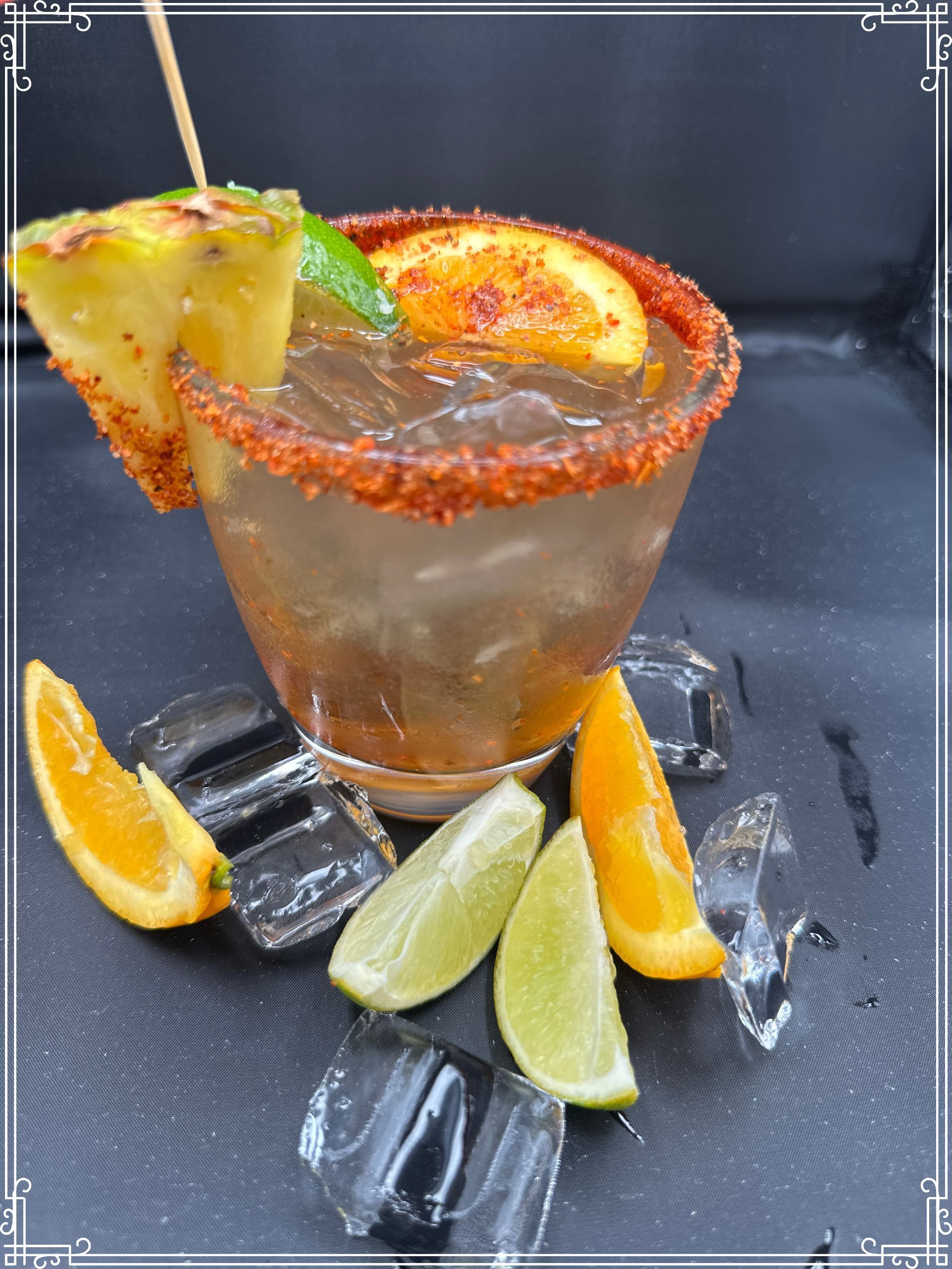 Cocktail with orange and lime garnishes, rimmed with red spice, on ice.