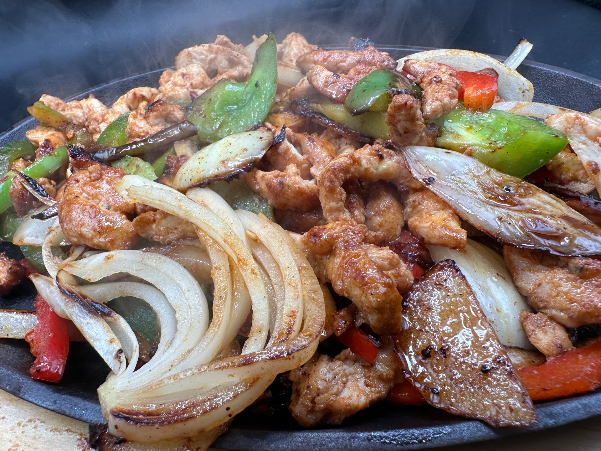 Sizzling chicken fajitas with onions and peppers on a hot cast iron platter.