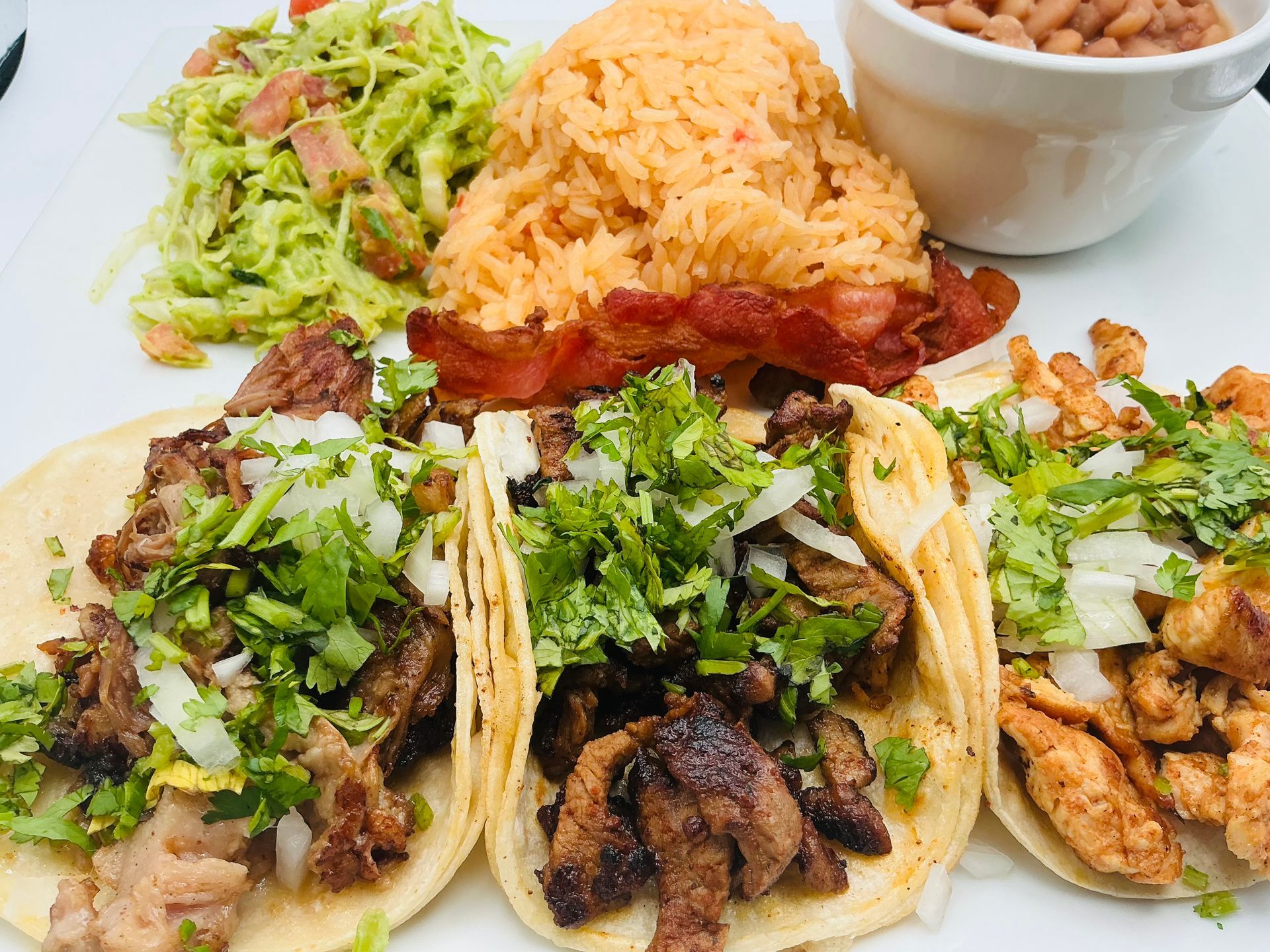 Plate of Mexican food: tacos with toppings, rice, beans, and guacamole.