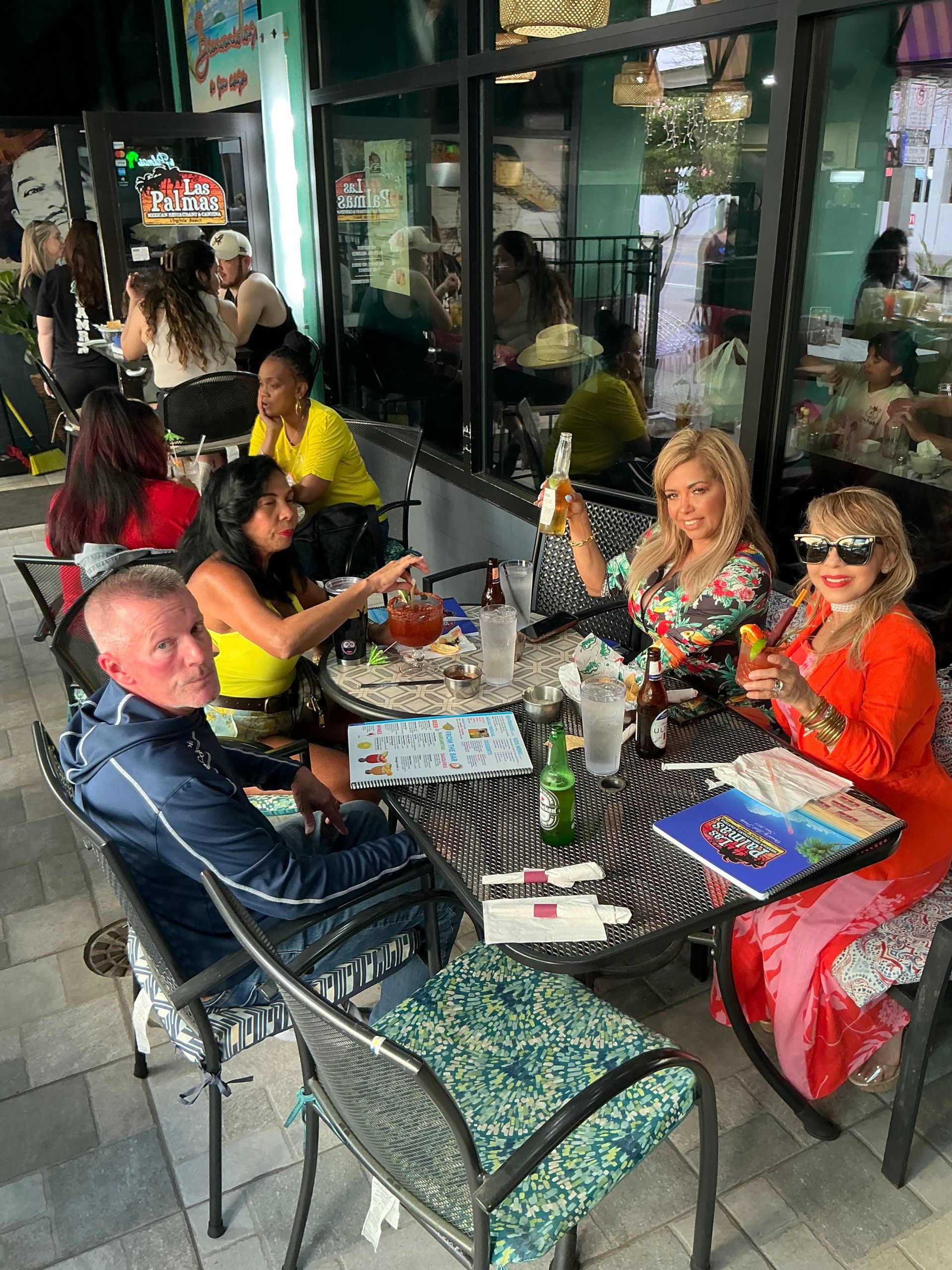 Outdoor restaurant patio scene. People are seated at tables, some eating, drinking, and talking.