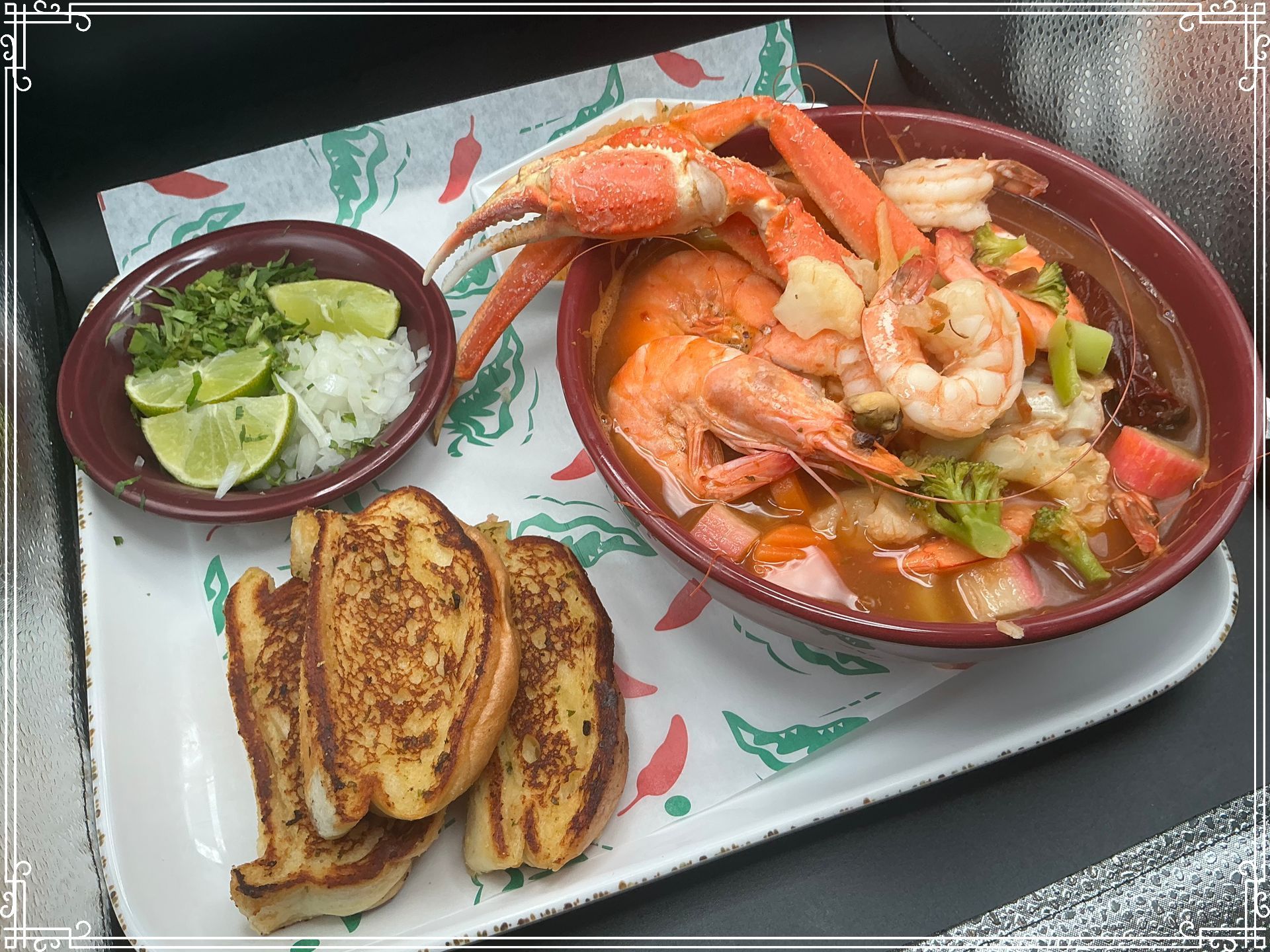 Seafood soup with shrimp, crab legs, and vegetables, served with lime, onions, and toast.