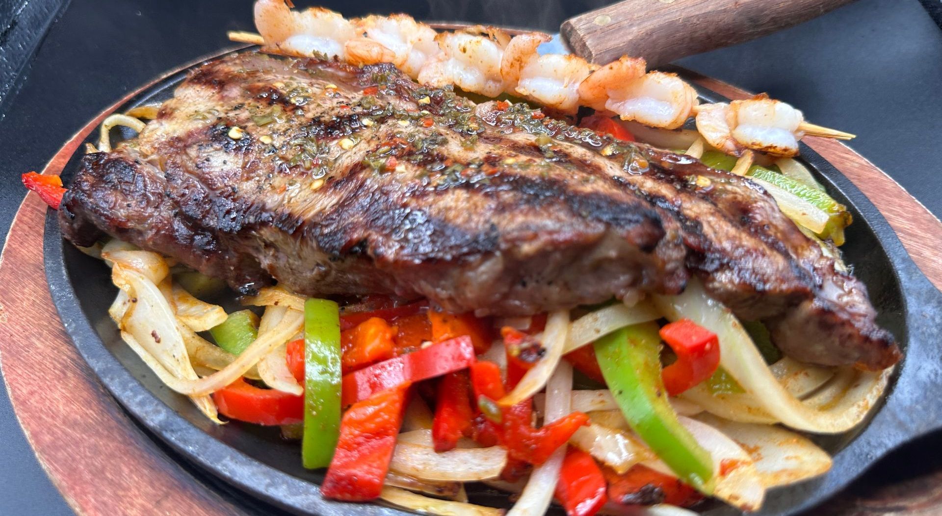 Sizzling steak and shrimp skewers atop sauteed peppers and onions, served on a hot skillet.