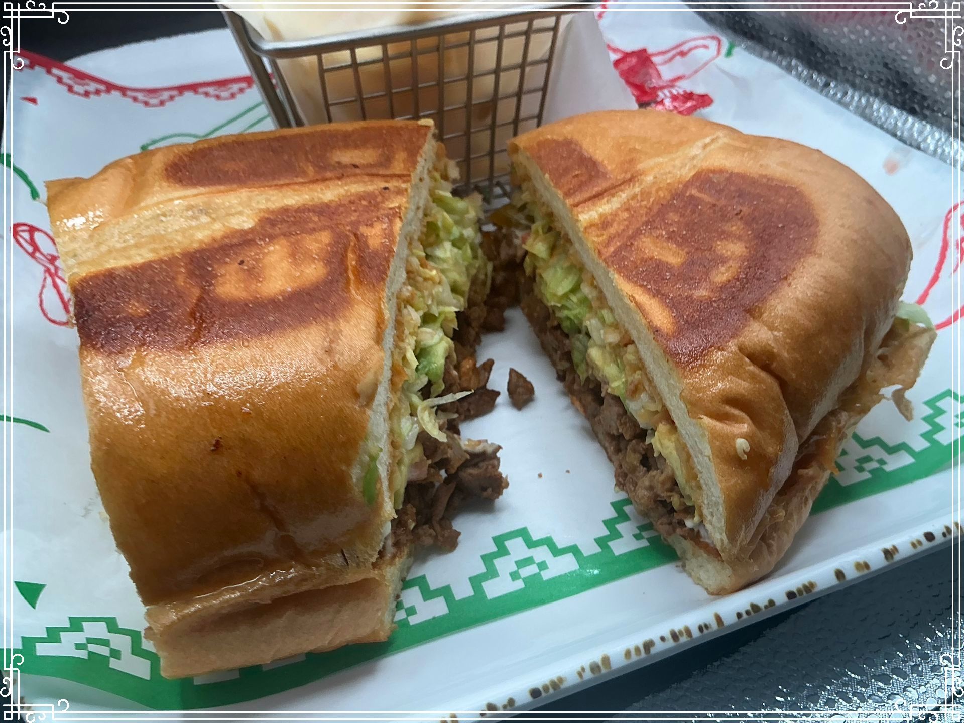 Halved sandwich with meat, avocado, and coleslaw on a white plate with a side of fries.