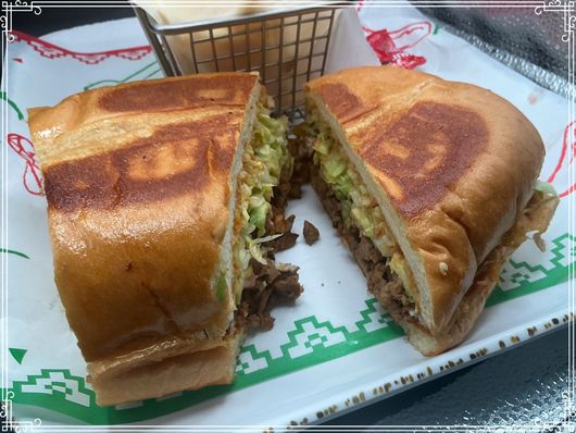 Halved sandwich with meat, avocado, and coleslaw on a white plate with a side of fries.
