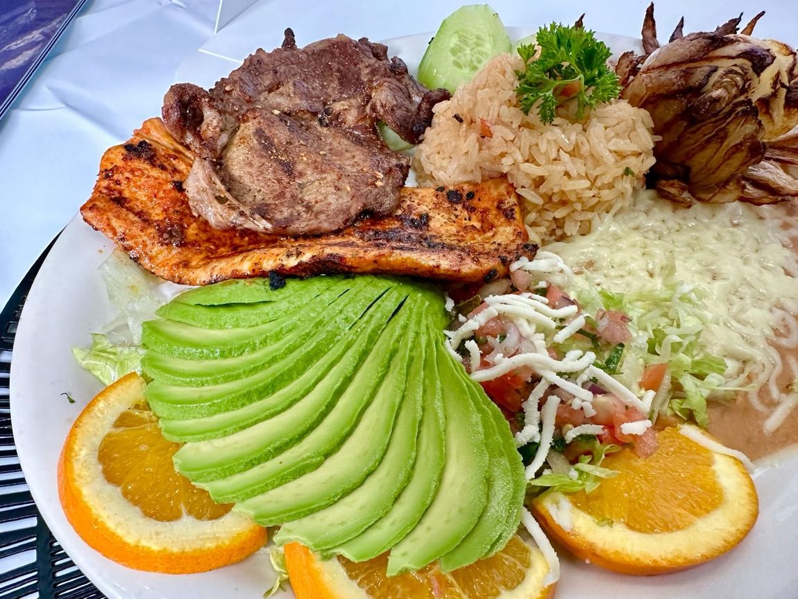 Plate with grilled meat, rice, beans, avocado, orange slices, and garnish.