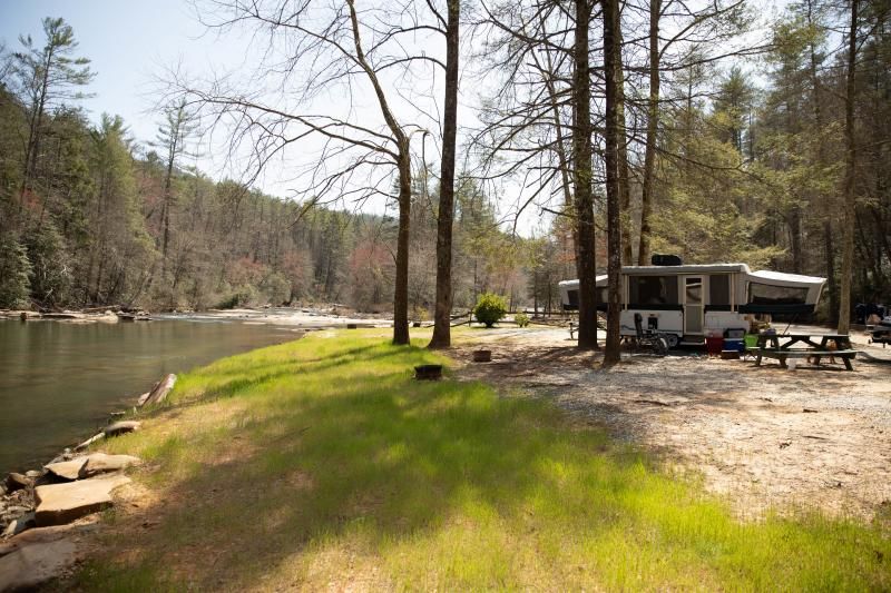 Riverside campsite with an RV, picnic table, and trees beside a calm river