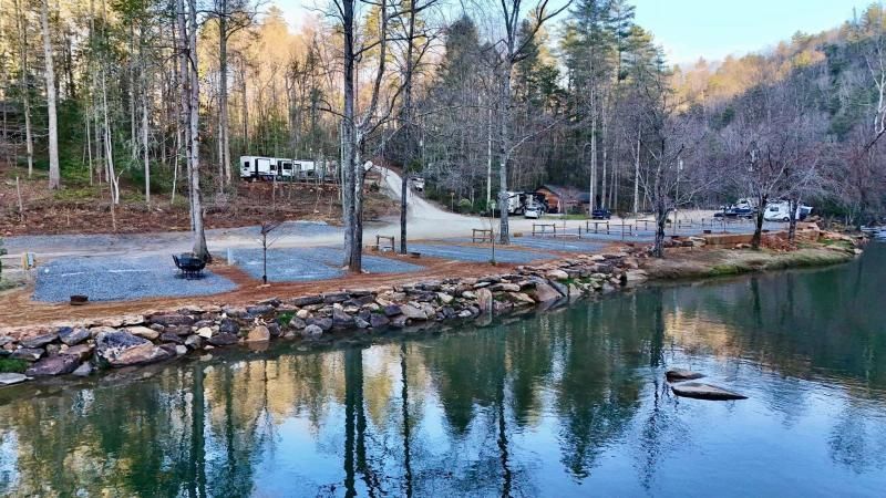 Calm lakeside park with trees, rocks, and a small dock reflecting in the water