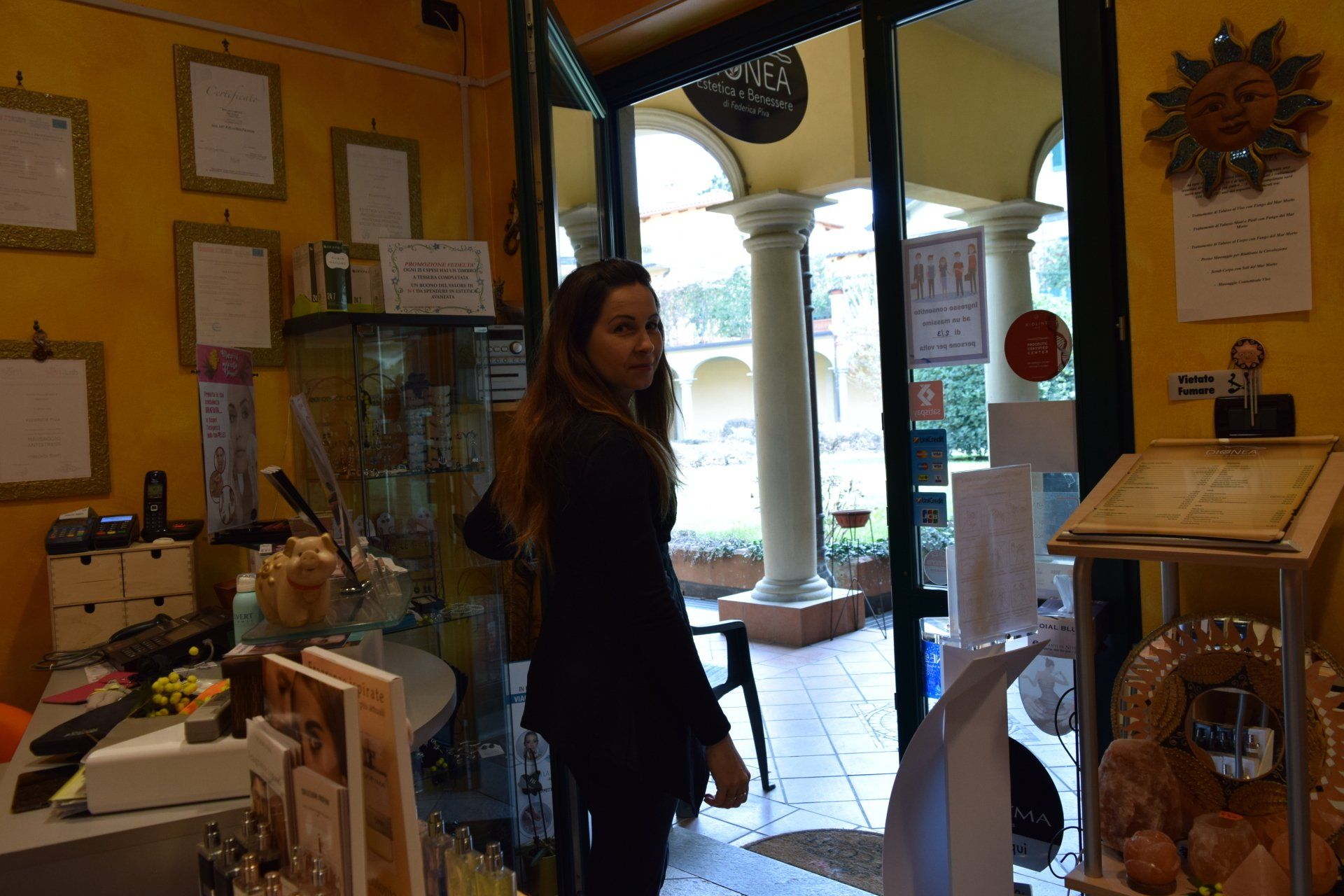 Donna in piedi vicino alla porta, che guarda indietro. All'interno di un locale con pareti gialle.
