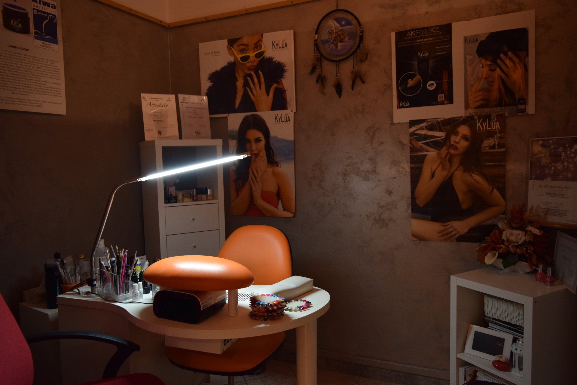 Interno di un salone per unghie con scrivania, sedia arancione, poster e lampada da scrivania.