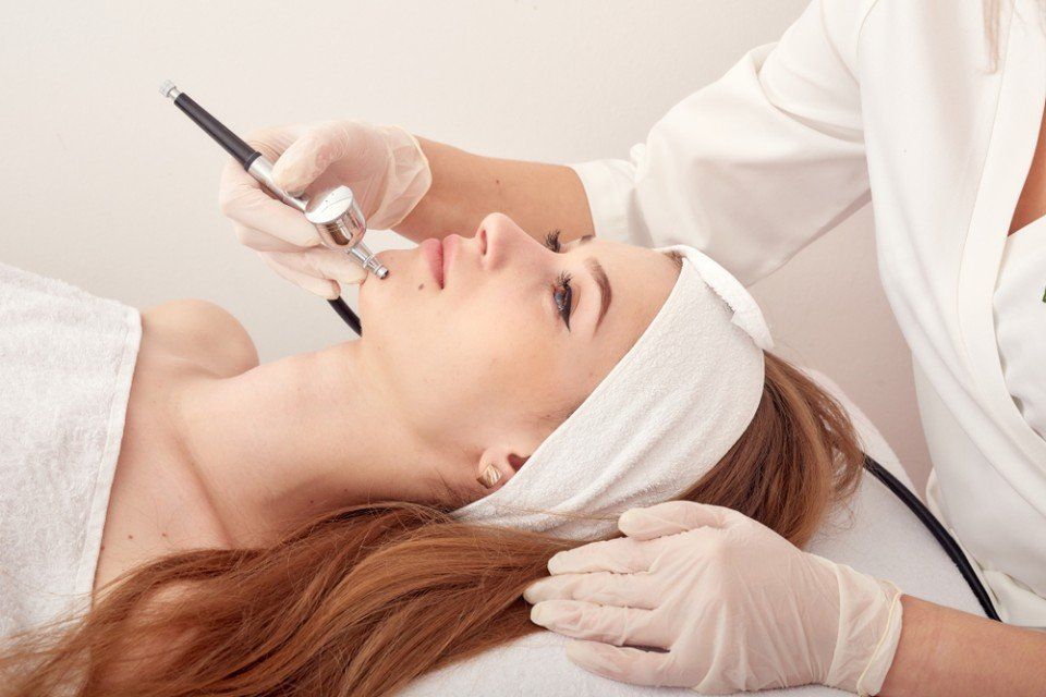 Donna che riceve un trattamento viso; l'estetista le tiene il dispositivo sul viso e indossa i guanti.