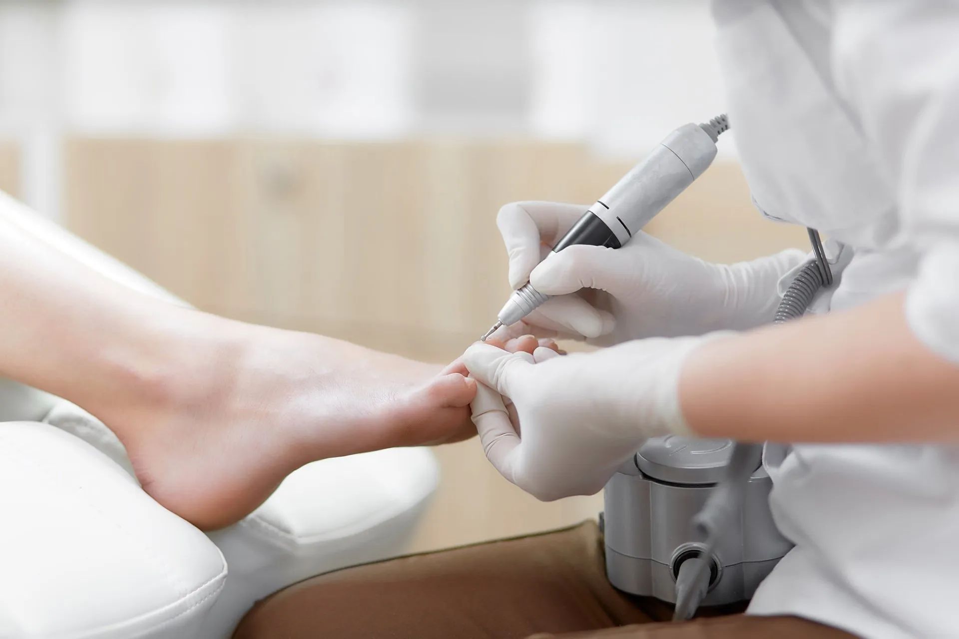 Piede di una persona che riceve una pedicure; strumento utilizzato sulle unghie dei piedi. All'interno, guanti bianchi.