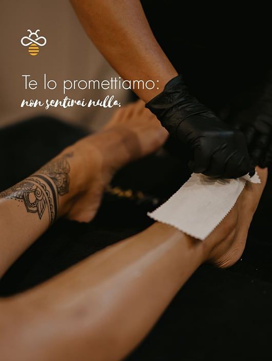 Gambe di una persona sottoposta a ceretta. Una gamba ha un tatuaggio. Vengono utilizzati guanti neri e carta bianca.