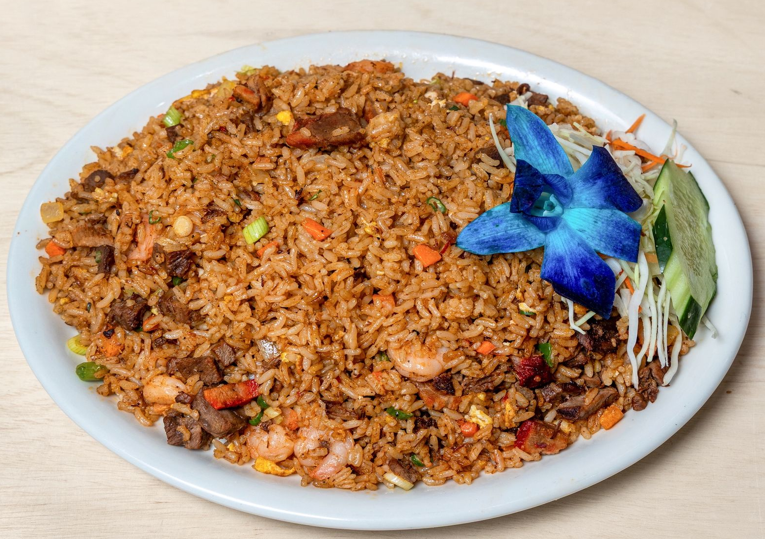 Fried rice with shrimp and meat, garnished with a flower and cucumber on a white plate.