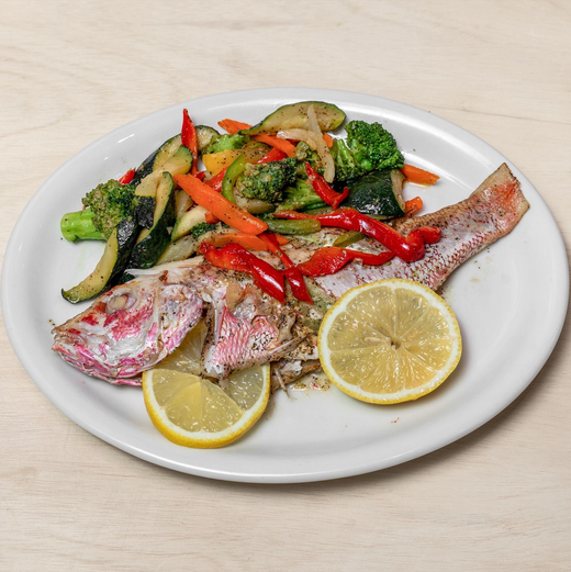 Grilled fish with vegetables and lemon slices on a white plate.