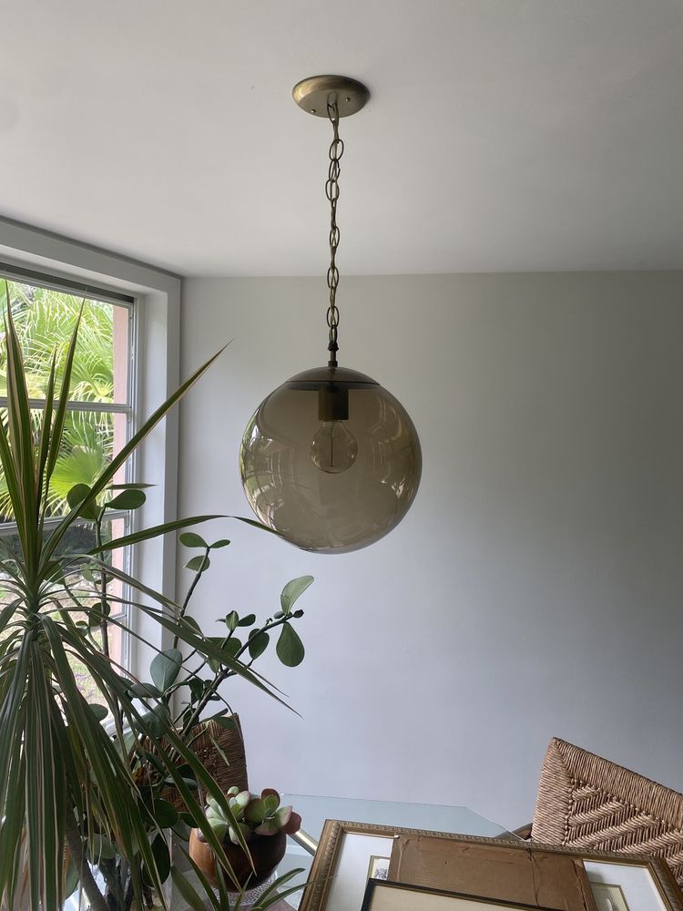 A round, smoky glass pendant light hangs from the ceiling. Plants and art are in the room.