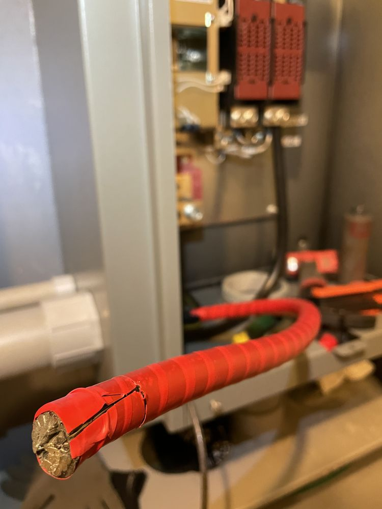 Red electrical wire with exposed copper end, bent in a curve, near a gray panel.