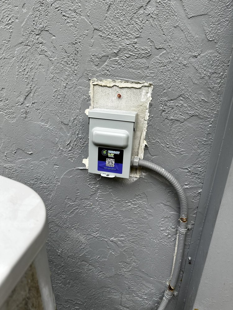 Gray electrical box mounted on a textured gray wall, with a flexible conduit leading to it.