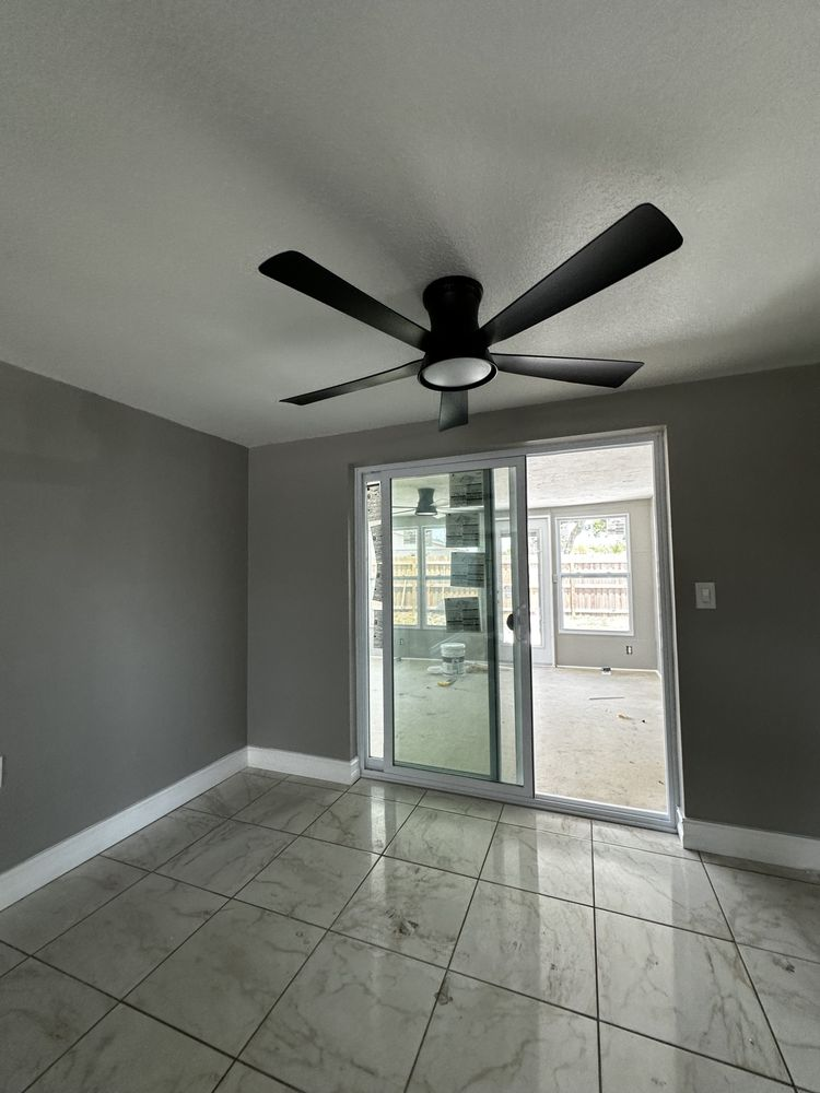 Empty room with gray walls, tiled floor, sliding glass door, and black ceiling fan.