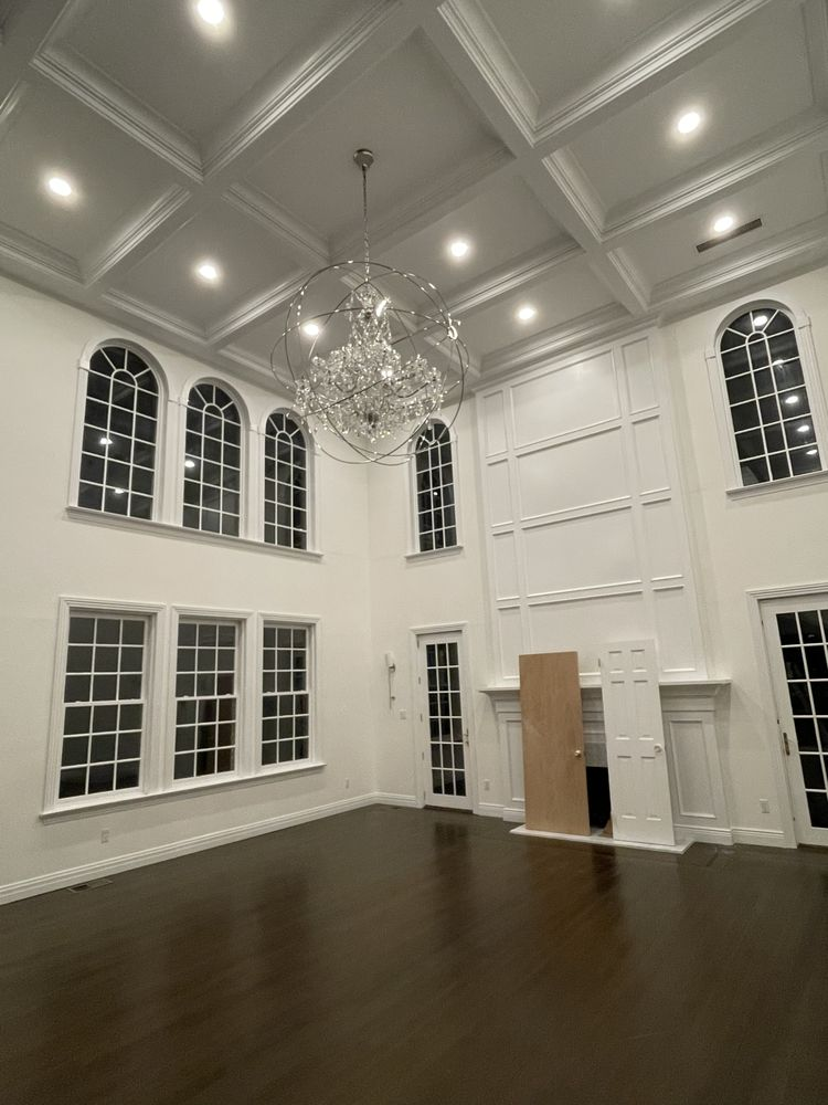 Spacious, empty room with high ceilings, large windows, chandelier, and dark wood floors.