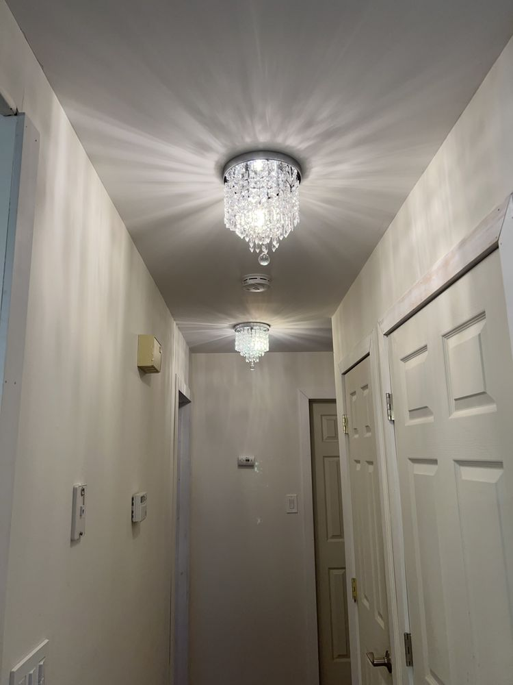 A hallway with two crystal chandeliers centered on the ceiling, white walls, and white doors.