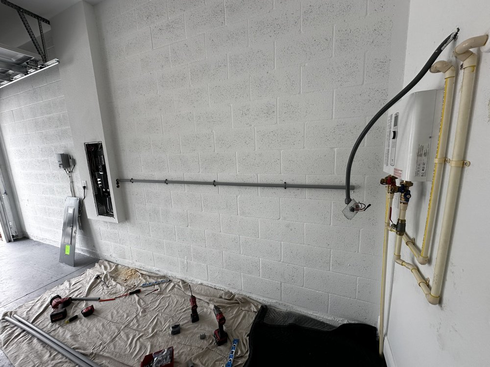Garage interior with exposed brick wall, gas water heater, and electrical work in progress.