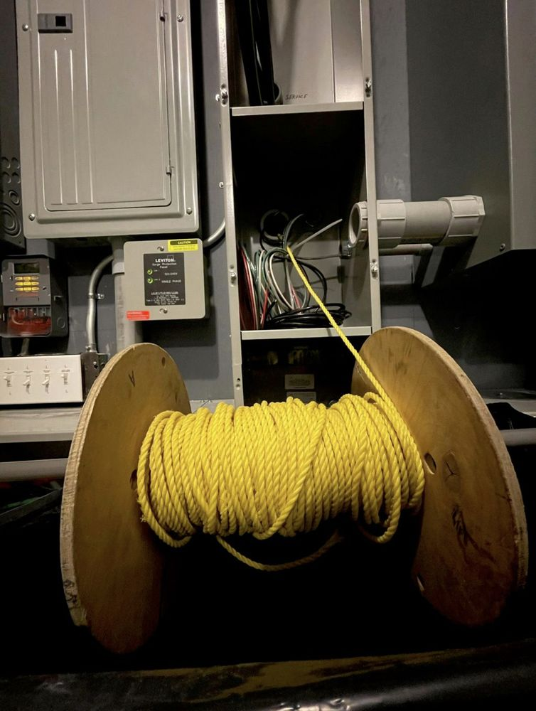 Wooden spool of yellow rope in front of electrical equipment and wiring.