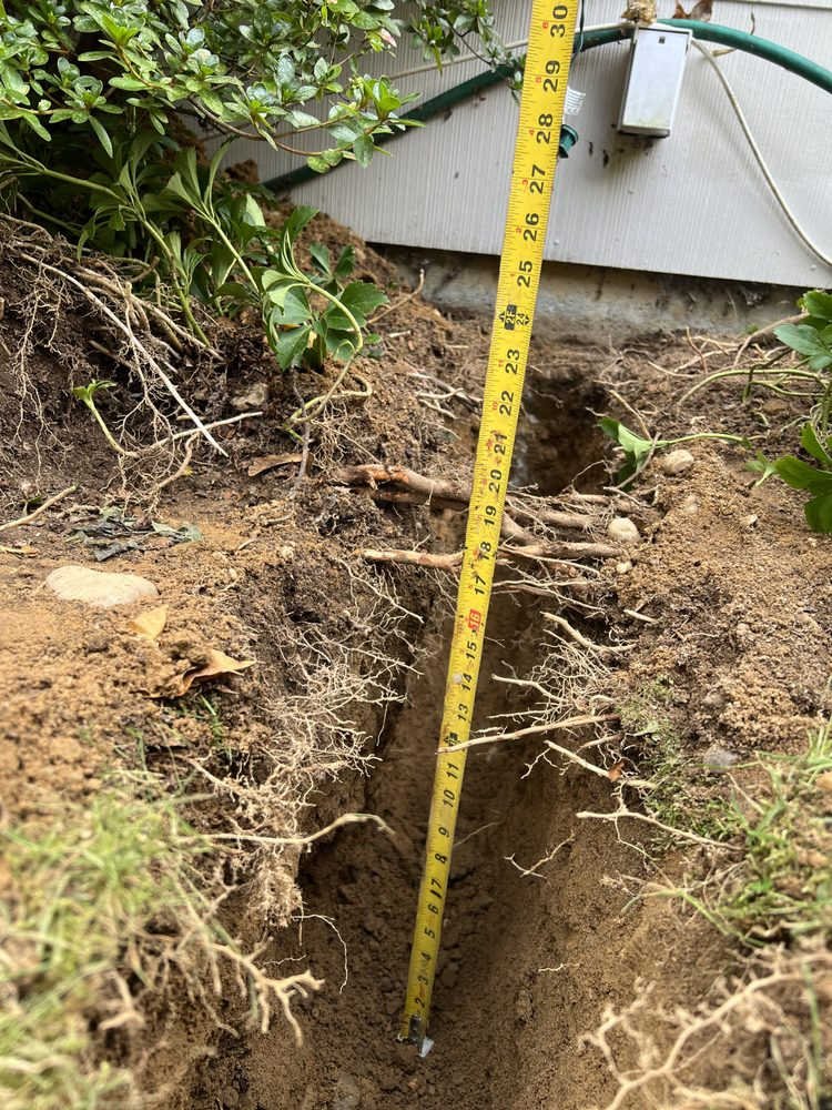 A hole in the ground next to a house with a measuring tape inside, showing depth.