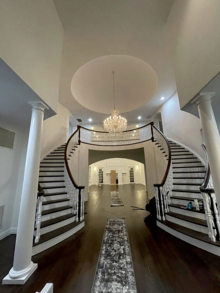 Grand foyer with dual curved staircases, chandelier, and a dark wood floor.