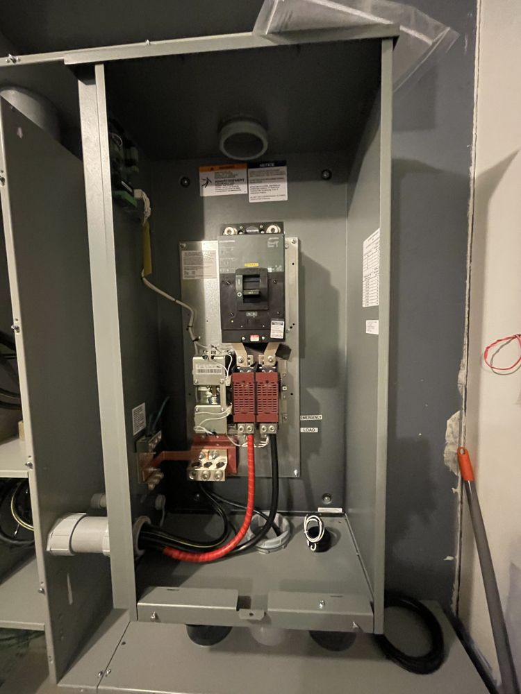 Gray electrical cabinet open, showing circuit breakers, wiring, and labels.
