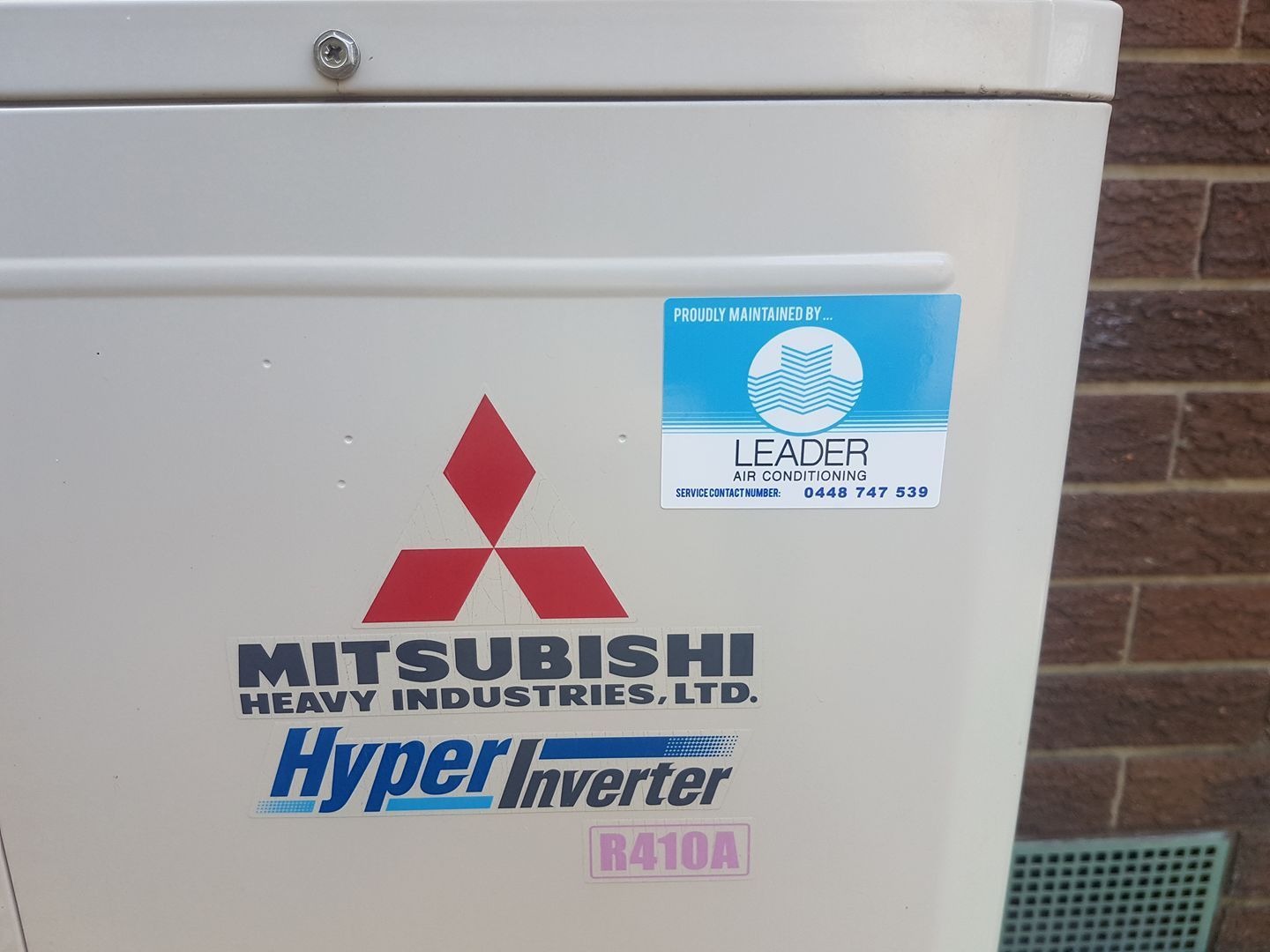 Mitsubishi air conditioning unit with logos and stickers, mounted on an exterior wall. — Leader Air Conditioning in Albury/Wodonga, VIC