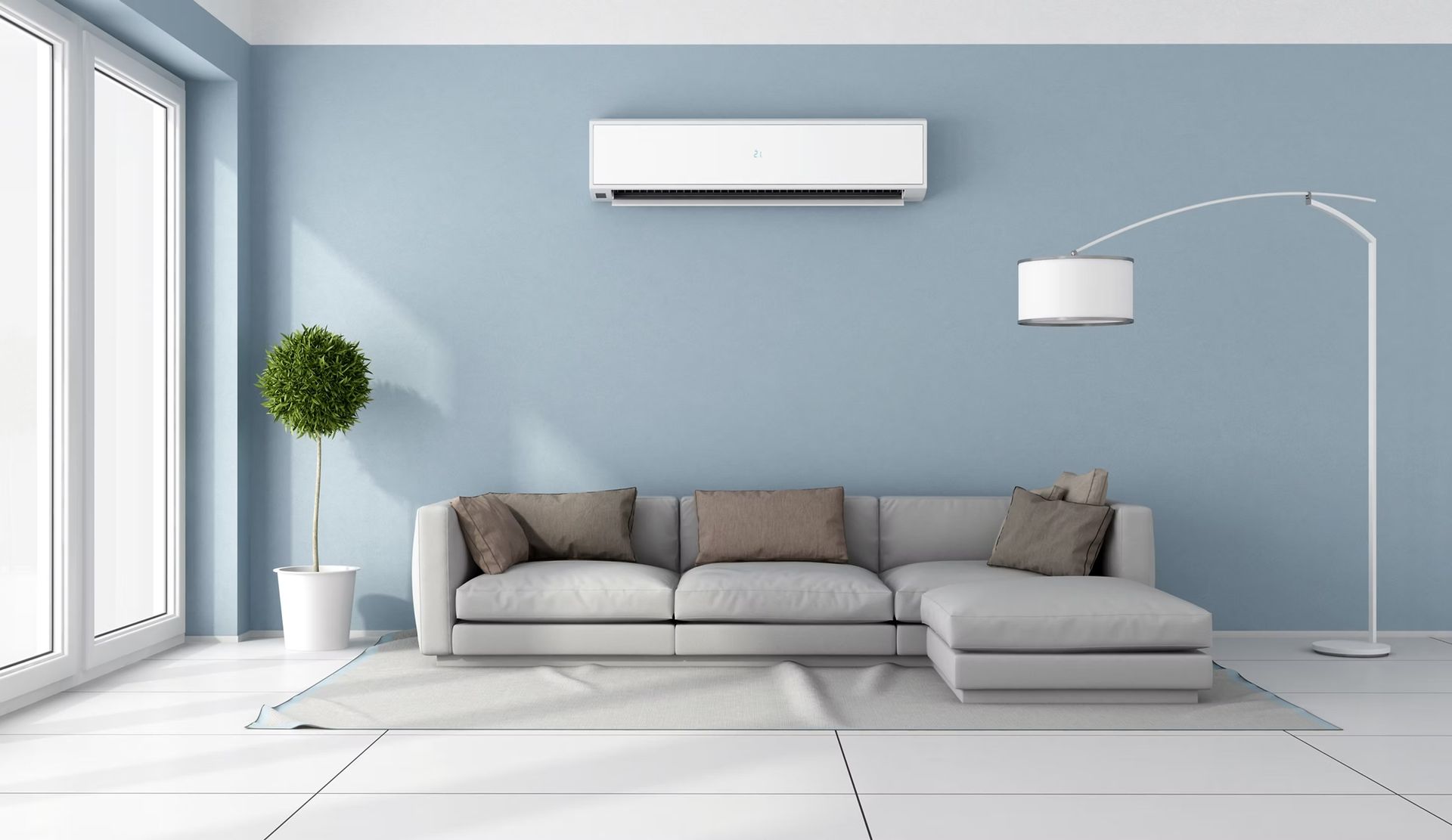 Blue-walled living room with a white couch, AC unit, floor lamp, and a small potted tree near a large window. — Leader Air Conditioning in Queanbeyan, NSW