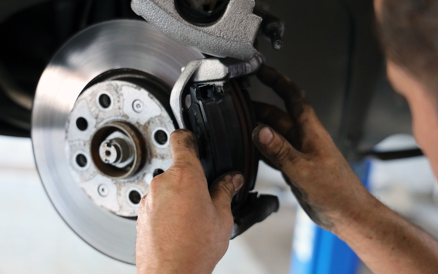 Mechanic replacing brake pads on a car wheel; close-up view of hands, disc, and caliper. | Jeremi's Auto Repair