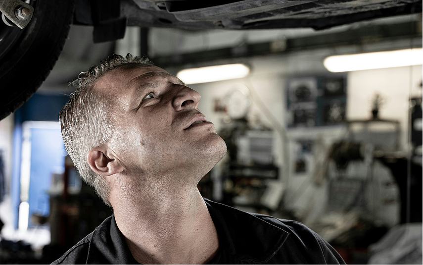 Mechanic inspecting the underside of a car in a garage. He looks up, focused. | Jeremi's Auto Repair