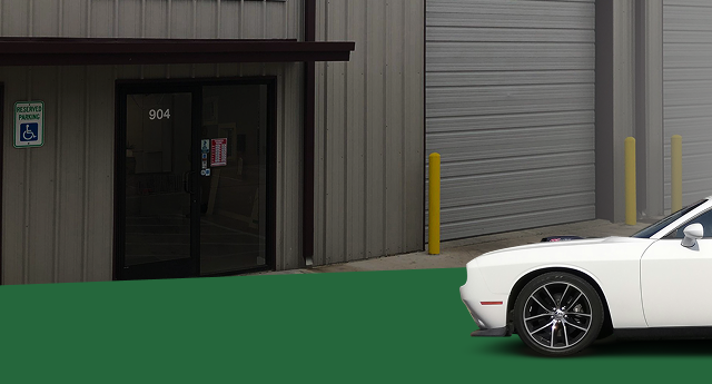 White car in front of a building with a handicap sign on the left. | Jeremi's Auto Repair