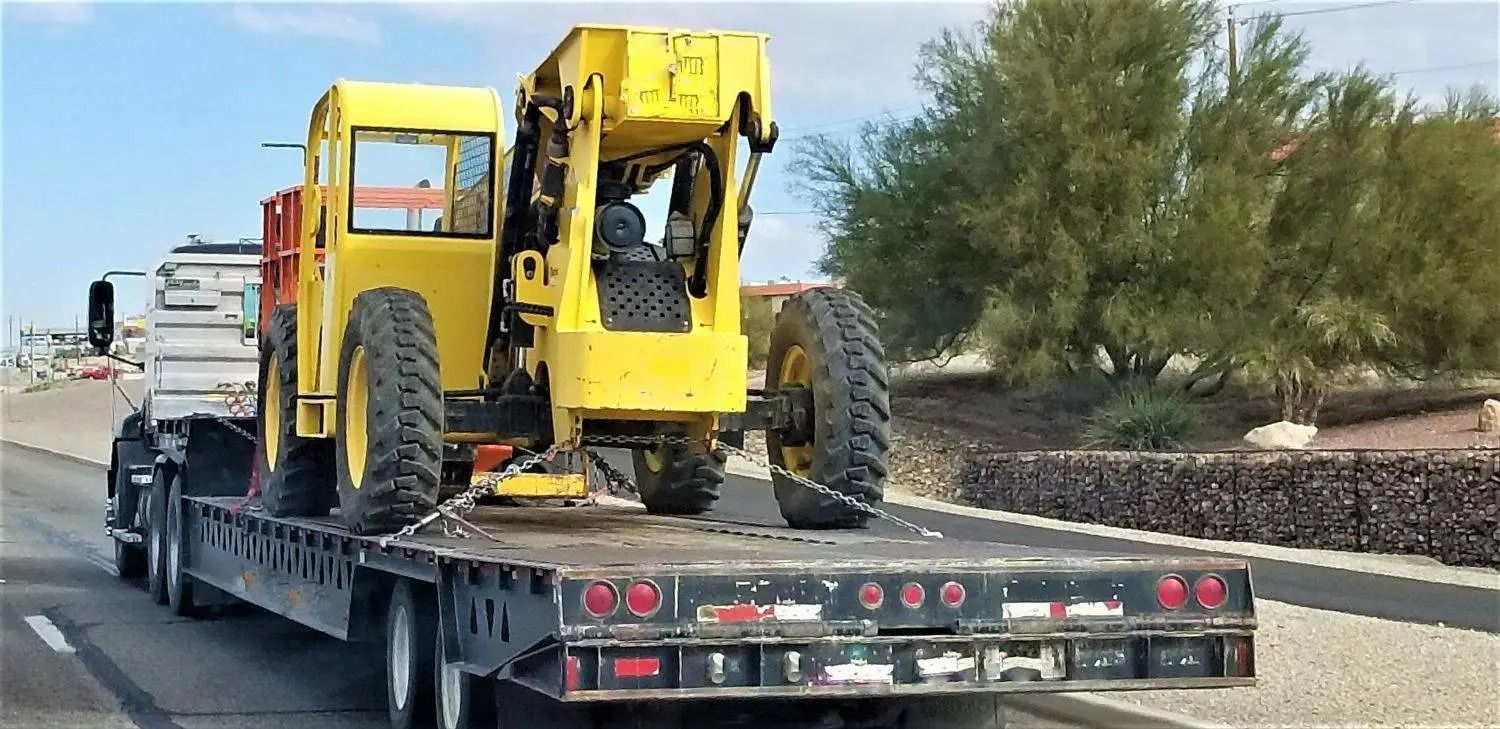 Yellow off-road vehicle strapped on a flatbed trailer on a road beside desert trees