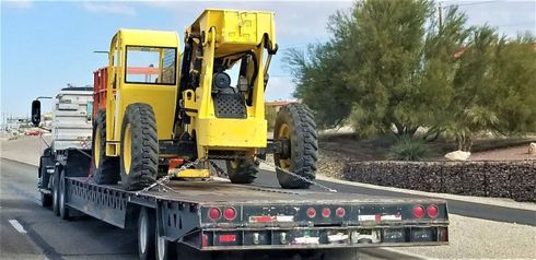Yellow off-road vehicle strapped on a flatbed trailer on a road beside desert trees