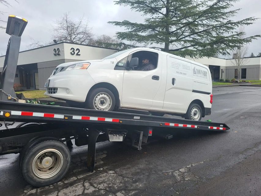White cargo van on a flatbed tow truck in a parking lot near office buildings.