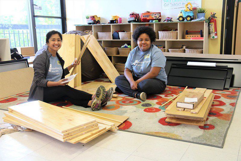 Two people sitting on a rug in a classroom with wooden blocks and craft materials