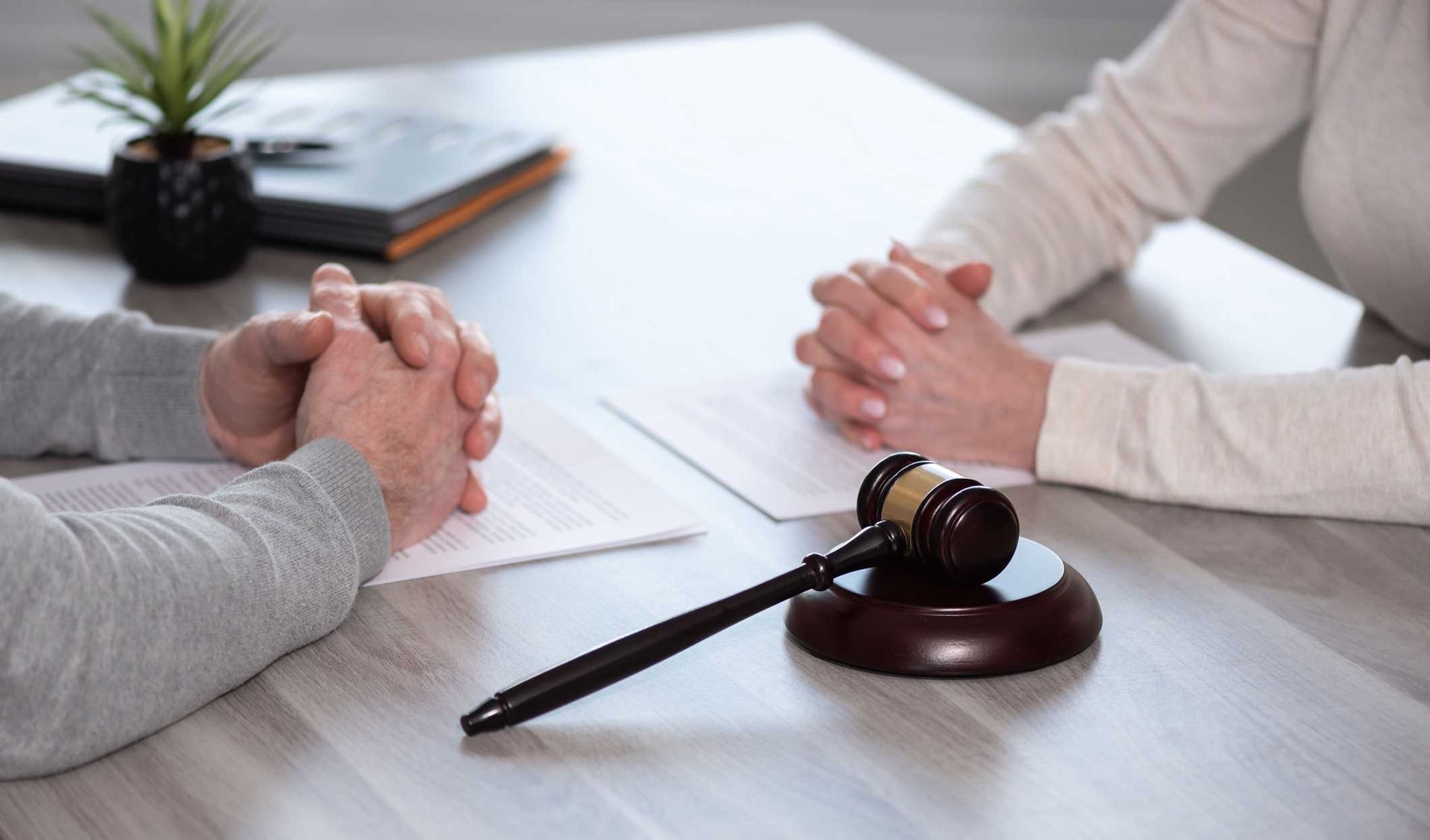Two people sitting across from each other at a table with a judge's gavel and legal documents