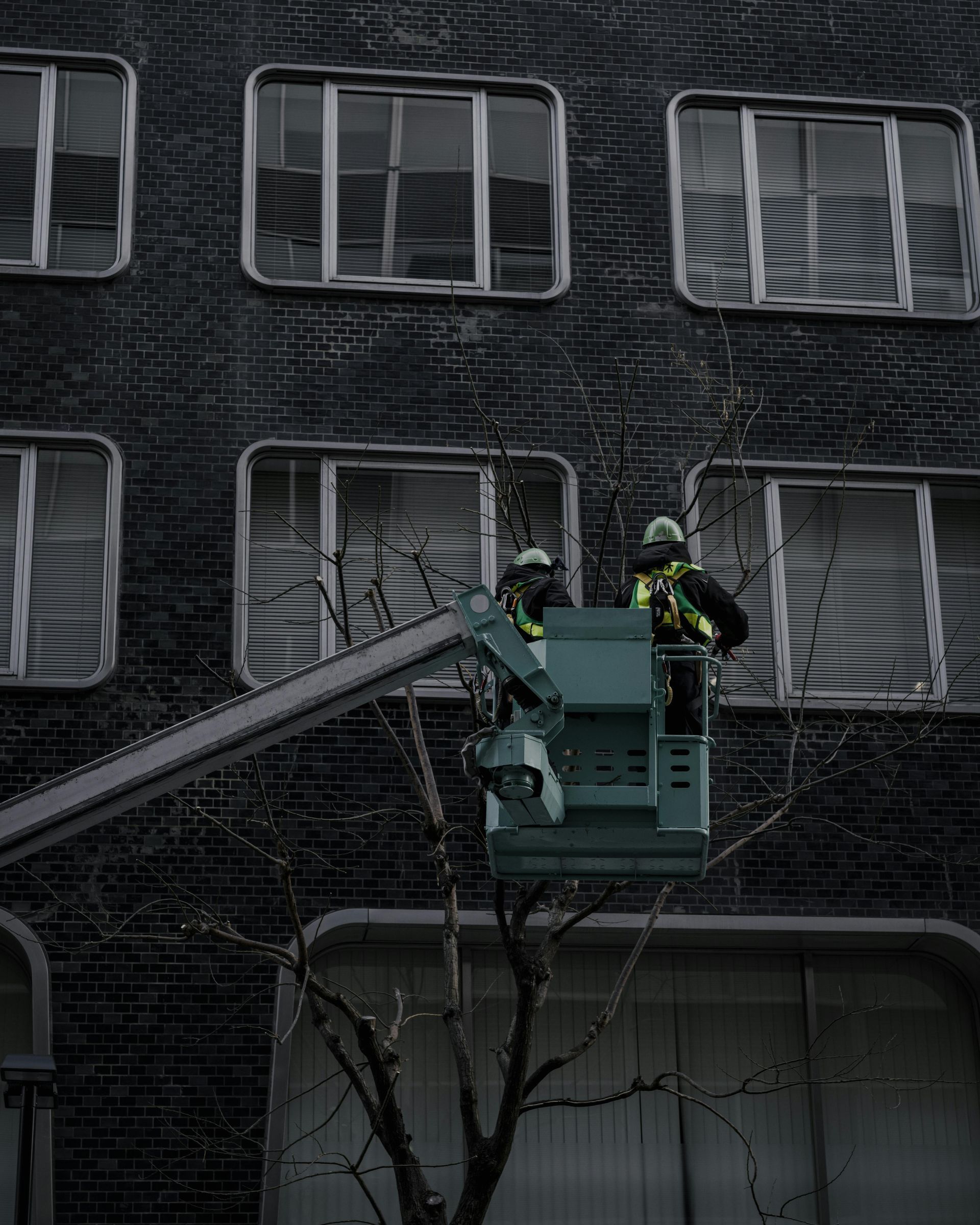 Two workers in a boom lift working on a dark brick building with barred windows