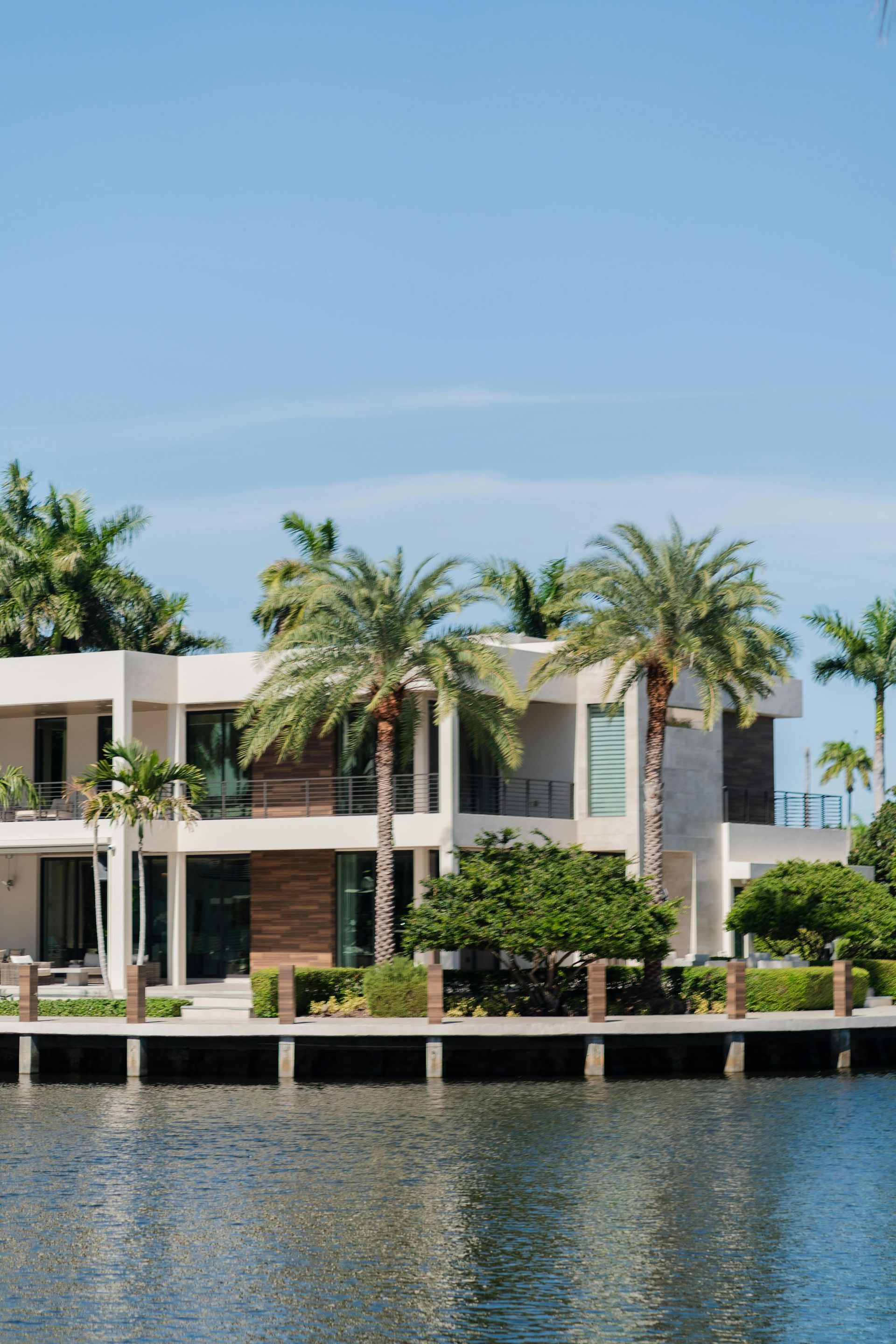 Modern waterfront house with palm trees and a calm blue canal under a clear sky