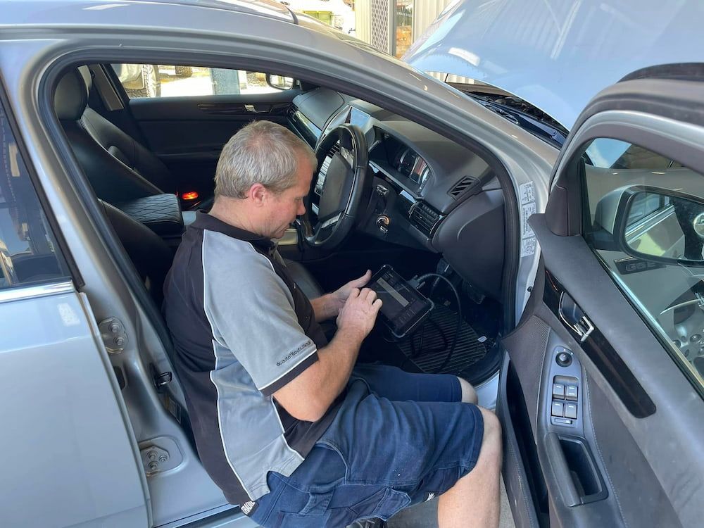 A Man Is Sitting In The Drivers Seat Of A Car Using A Tablet — Mudgeeraba Auto Electrical & Mechanical In Mudgeeraba, QLD